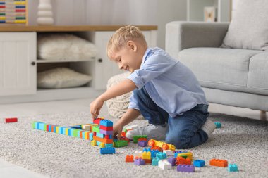 Mutlu küçük çocuk evde renkli oyuncak tuğlalarla oynuyor.