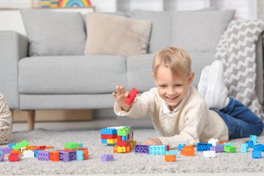 Mutlu küçük çocuk evde renkli oyuncak tuğlalarla oynuyor.