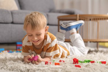 Mutlu küçük çocuk evde renkli oyuncak tuğlalarla oynuyor.