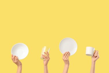 Sarı arka planda beyaz tabak, kase, bardak ve cam kaplı kadın elleri.