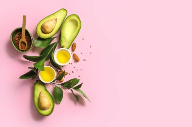 Taze avokado, bir kase yağ, keten tohumu ve pembe arka planda bitki dalları içeren kompozisyon