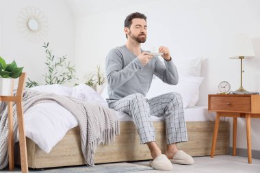 Sabah, elinde kahve fincanı olan yakışıklı bir adam yatak odasında oturuyor.