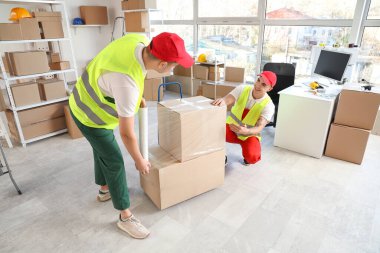 Erkek yükleyiciler depoda streç film kutularını paketliyor.