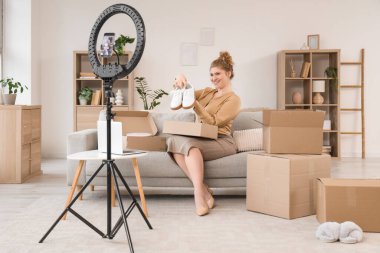 Evde video kaydedilirken yeni spor ayakkabılarla paket kutusunu açan genç bir kadın.