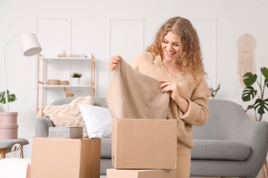 Evde yeni bir etekle paket kutusunu açan genç bir kadın.