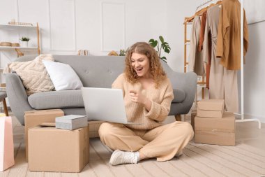 Dizüstü bilgisayarı ve paket kutusu olan genç bir kadın evde online alışveriş yapıyor.