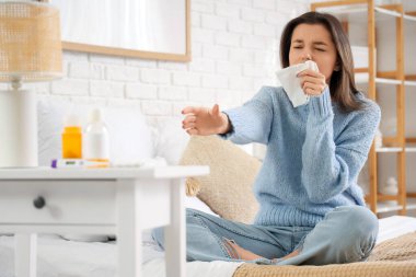 Yatak odasındaki masada öksürük şurubuyla hapşıran genç kadın.