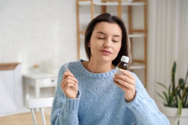 Yatak odasında öksürük şurubu olan genç bir kadın.