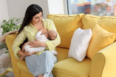 Evdeki kanepede oturan bir kadın bebeğini emziriyor.