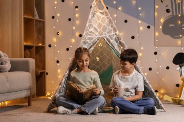 Geceleri çadırda macera kitabı okuyan sevimli çocuklar.