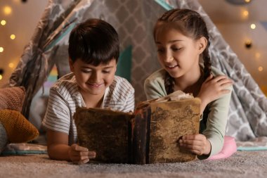Geceleri çadırda macera kitabı okuyan sevimli çocuklar.