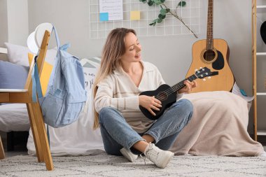 Yatak odasında halıda ukulele çalan genç bir kadın.