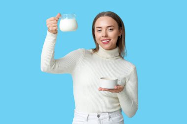 Bir fincan sıcak kahve ve mavi arka planda bir sürahi taze sütle güzel bir genç kadın.