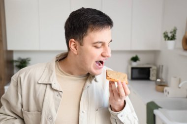 Genç adam mutfakta fıstık ezmeli tost yiyor.
