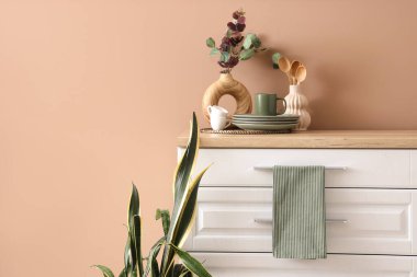 Okaliptüslü vazo, mutfaktaki bej duvarın yanındaki çekmecede bulaşık ve peçete.