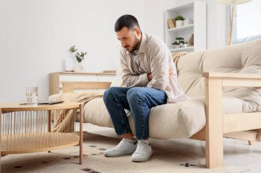 Evdeki kanepede karın ağrısı çeken genç bir adam.