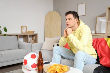 Evde Alman bayrağı taşıyan erkek sporcular futbol maçı izliyor.