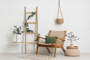 Hasır koltuk, merdiven ve okaliptüs dallı kahve masası. Odada beyaz tuğla duvarın yanında.