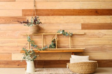 Merdiven, bank, yastıklı sepet ve okaliptüs dalları odasındaki ahşap duvarın yanında.