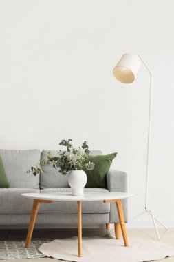 Konforlu kanepe, okaliptüs dallı sehpa vazoda beyaz duvarın yanında lamba.