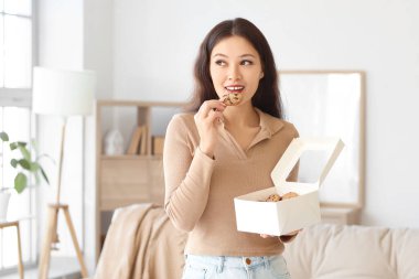 Evde bir kutu kurabiyesi olan genç Asyalı kadın.