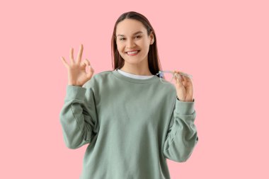 Yeni gözlüklü güzel, genç ve mutlu bir kadın pembe arka planda güzel bir jest yapıyor.