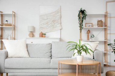 Aydınlık oturma odasının içinde gri kanepe ve masa üzerinde bitki var.