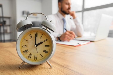 Ofiste çalışan işadamına karşı masada antika çalar saat.