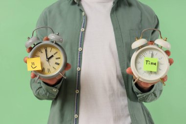 Alarm saatlerini tutan adam Kelime Time ve kağıttan gülücük yeşil arka planda, yakın plan
