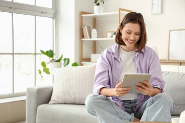 Evdeki kanepede tablet bilgisayar kullanan mutlu genç bir kadın.