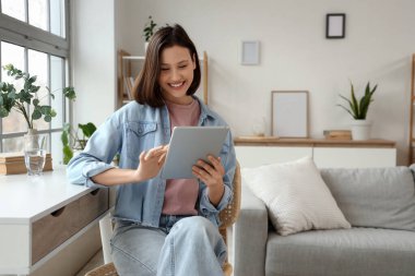 Evde tablet bilgisayar kullanan gülümseyen genç bir kadın.