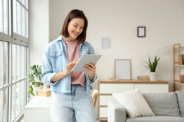 Evdeki pencerenin yanında tablet bilgisayar kullanan genç bir kadın