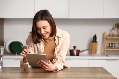Mutfaktaki masada tablet bilgisayar kullanan genç bir kadın.