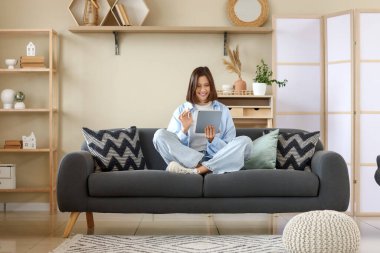 Evdeki koltukta modern tablet bilgisayar kullanan genç bir kadın.