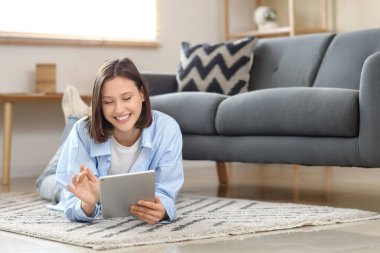 Evdeki halının üzerinde modern tablet bilgisayar kullanan genç bir kadın.