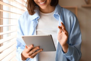 Evdeki pencerenin yanında modern tablet bilgisayar kullanan genç bir kadın.