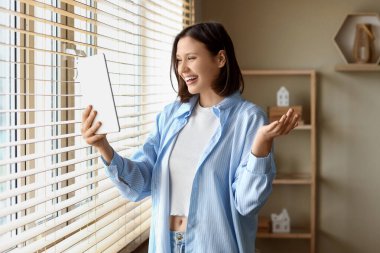 Genç bir kadın evdeki pencerenin yanında modern tablet bilgisayar kullanıyor.