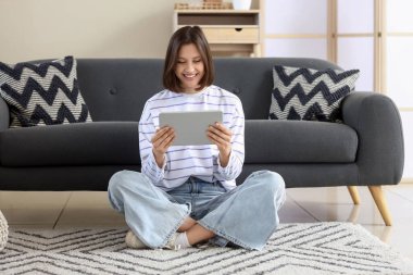 Evdeki halıda tablet bilgisayar kullanan genç bir kadın.