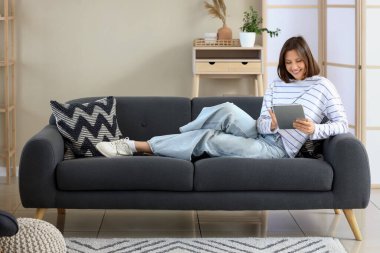 Evdeki koltukta tablet bilgisayar kullanan genç bir kadın.