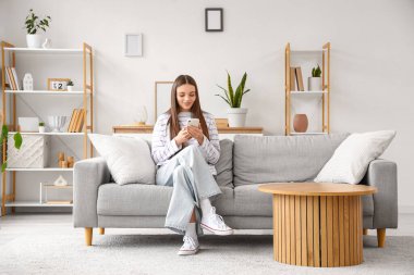 Evdeki koltukta cep telefonu kullanan genç bir kadın.