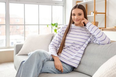 Evdeki gri kanepede oturan genç kadın.