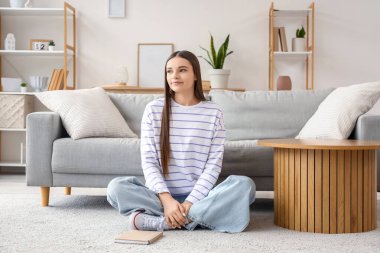 Evdeki halıda oturan genç kadın.