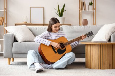 Evde gitar çalan genç bir kadın.
