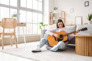 Evde gitar çalan genç bir kadın.