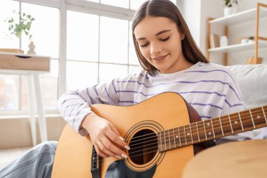 Evde gitar çalan genç bir kadın.