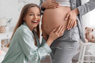 Genç lezbiyen kadın yatak odasında hamile karısının karnına dokunuyor.