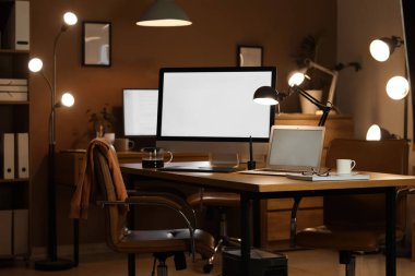Boş bilgisayar monitörü, dizüstü bilgisayarı ve parlak lambası olan bir işyeri.