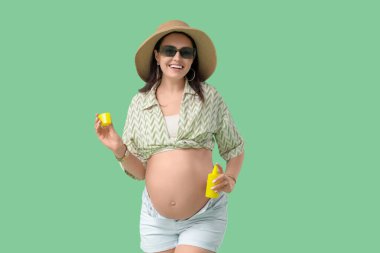 Yeşil arka planda güneş kremi şişesi olan hamile bir kadın. Seyahat kavramı
