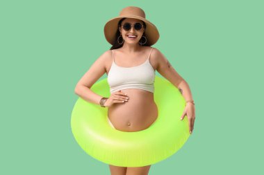 Yeşil arka planda şişme yüzüğü olan genç hamile bir kadın. Seyahat kavramı