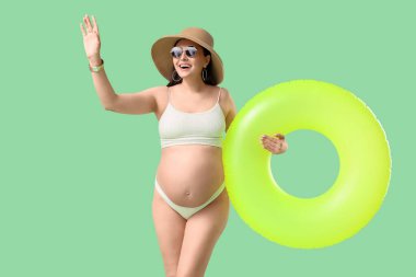 Yeşil arka planda şişme yüzüğü olan genç hamile bir kadın. Seyahat kavramı
